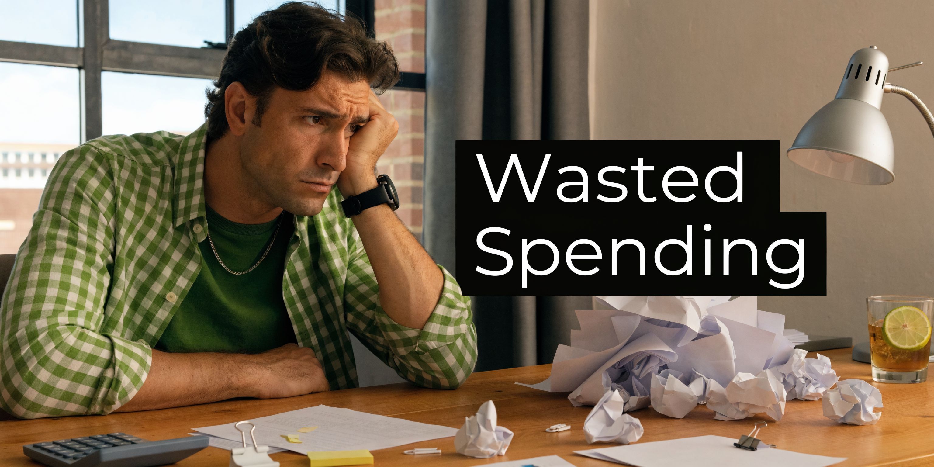 A frustrated man sits at a desk with crumpled papers, symbolizing the struggle of wasted business spending.