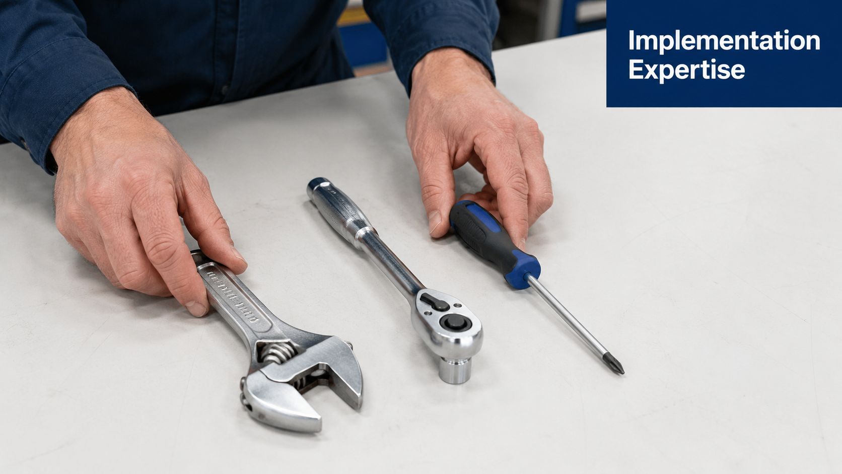 A technician sets a wrench, a ratchet, and a screwdriver on a clean white workbench surface.